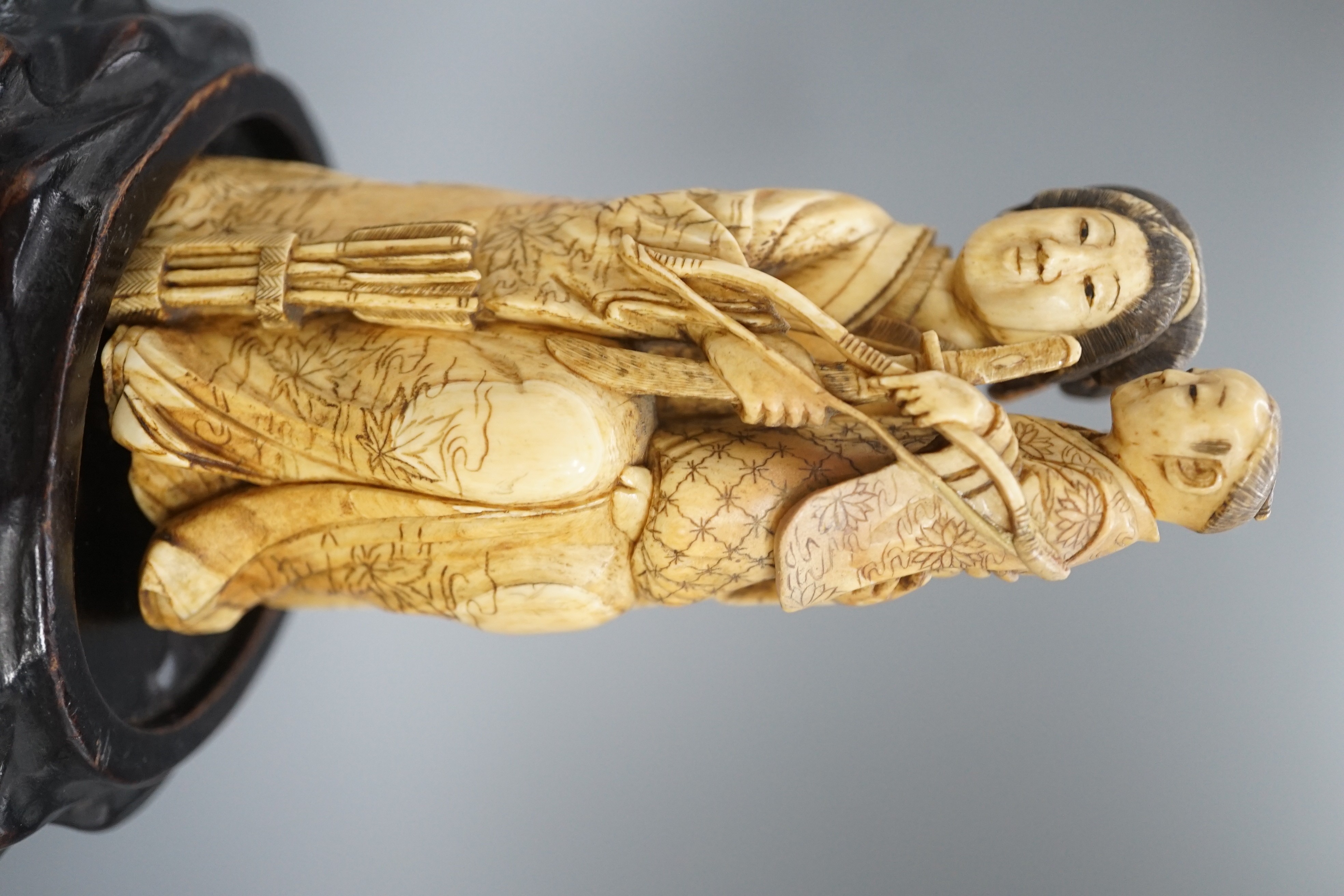 A Japanese ivory okimono of a lady holding a boy with a bow and arrow, Meiji period, restoration 12cm, wood stand
